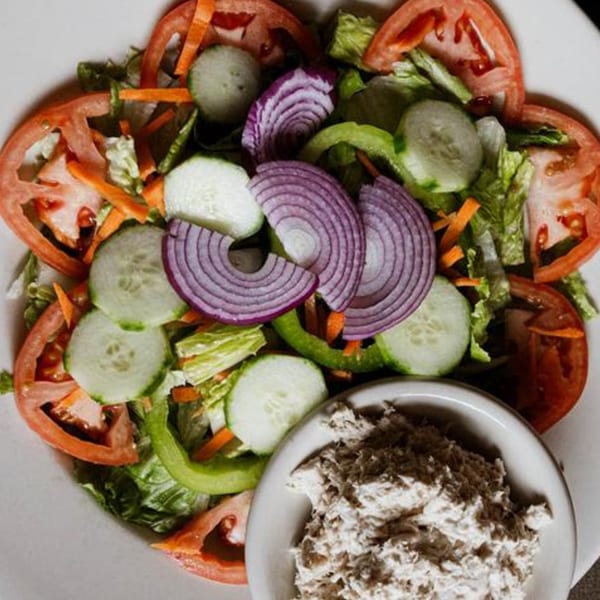A fresh garden salad with lettuce, tomatoes, cucumbers, onions, and bell peppers, served with tuna salad.