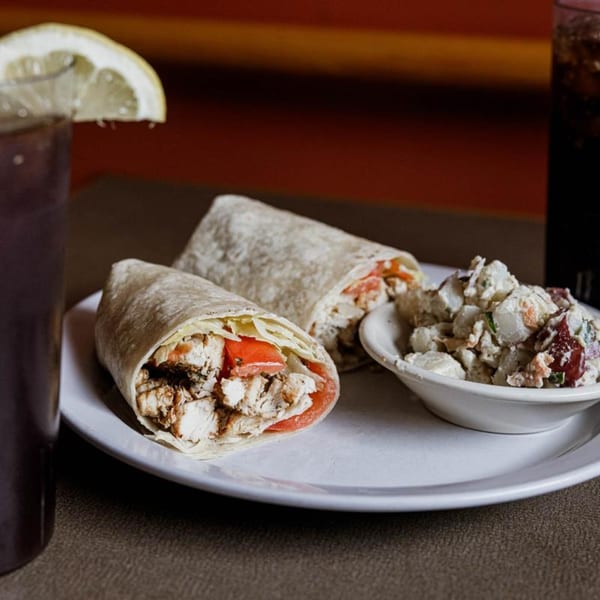 Two chicken wraps with tomato and lettuce, a side of potato salad, and iced tea with lemon.