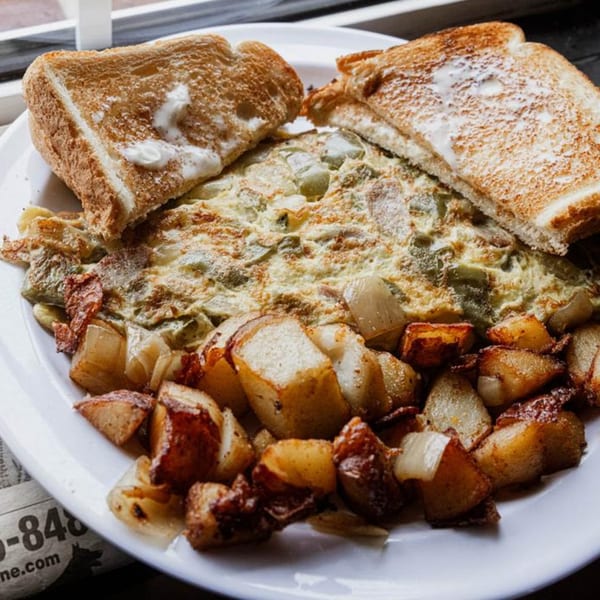 A breakfast plate with a cheesy omelet, crispy home fries, and buttered toast.