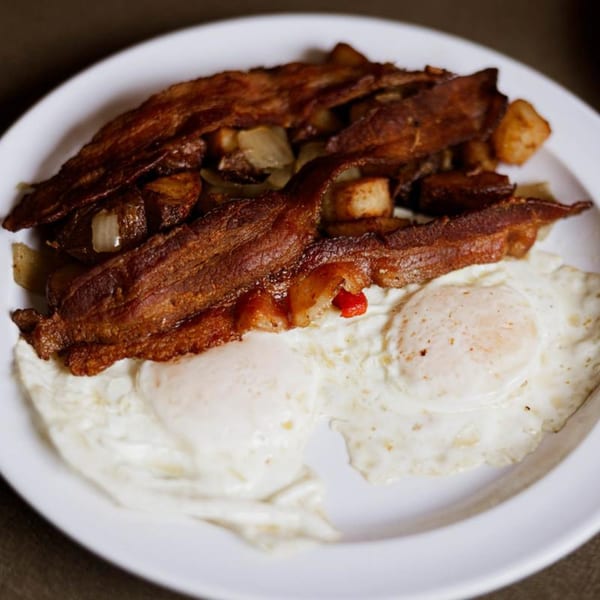 A breakfast plate with crispy bacon, home fries with onions, and two fried eggs.