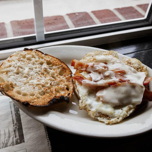 A breakfast sandwich with bacon, egg, and cheese on toasted bread, next to a window.