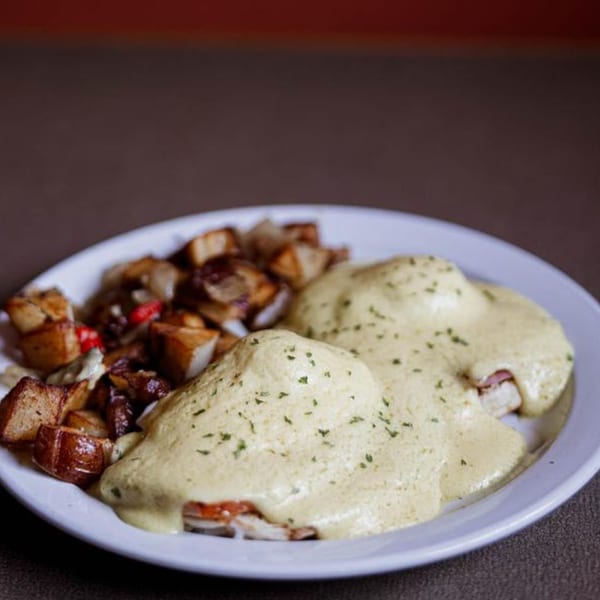 Eggs Benedict with hollandaise sauce and a side of roasted potatoes on a white plate.